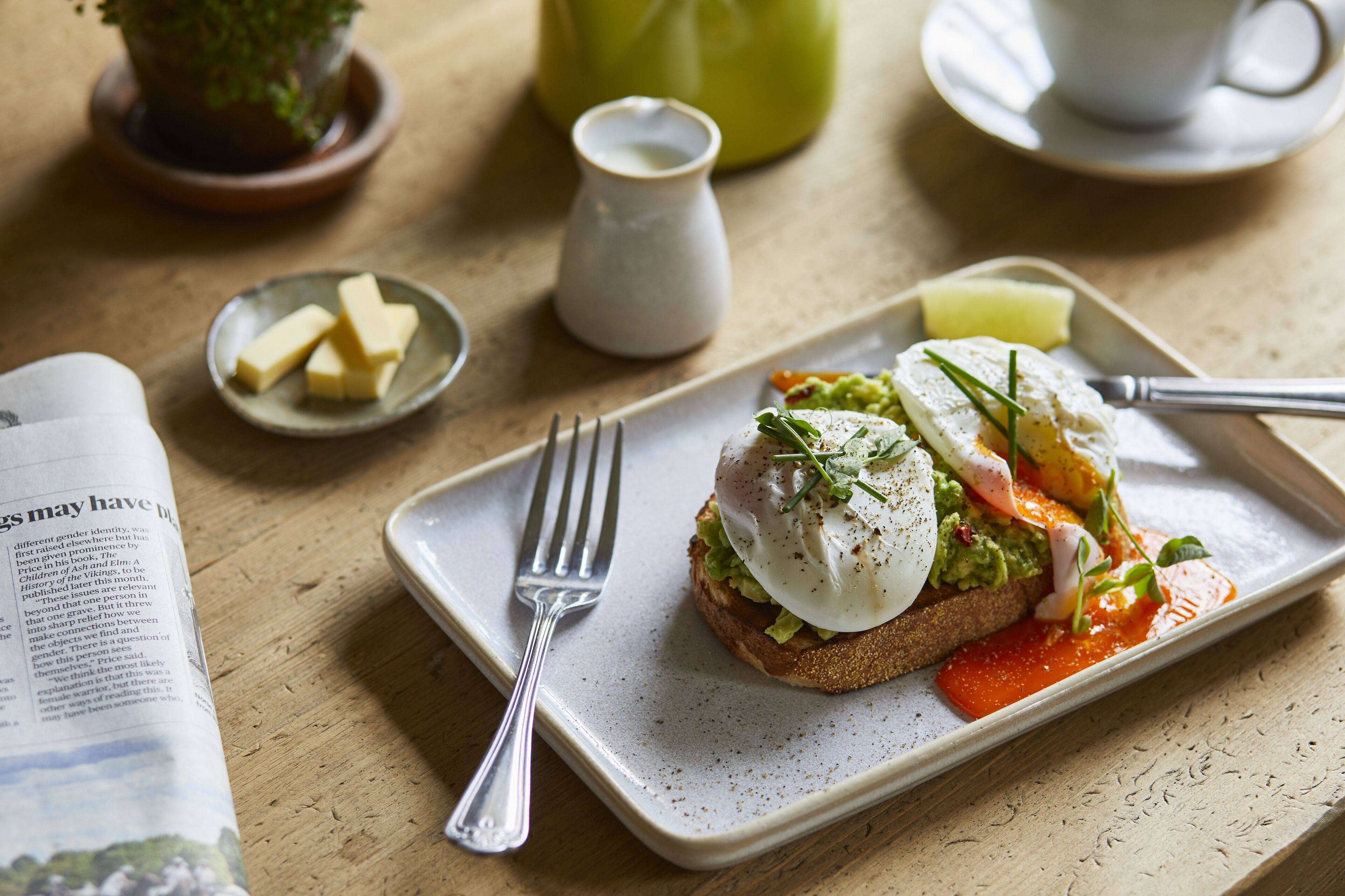 A breakfast plate with toast, eggs, and vegetables on a table with a book, a cup, and a pitcher.