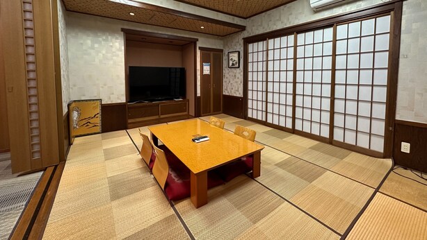 Une pièce de style japonais traditionnel, avec un sol recouvert de tatamis, une table basse en tatami, un téléviseur, des portes coulissantes et un plafond doté d’un éclairage encastré.