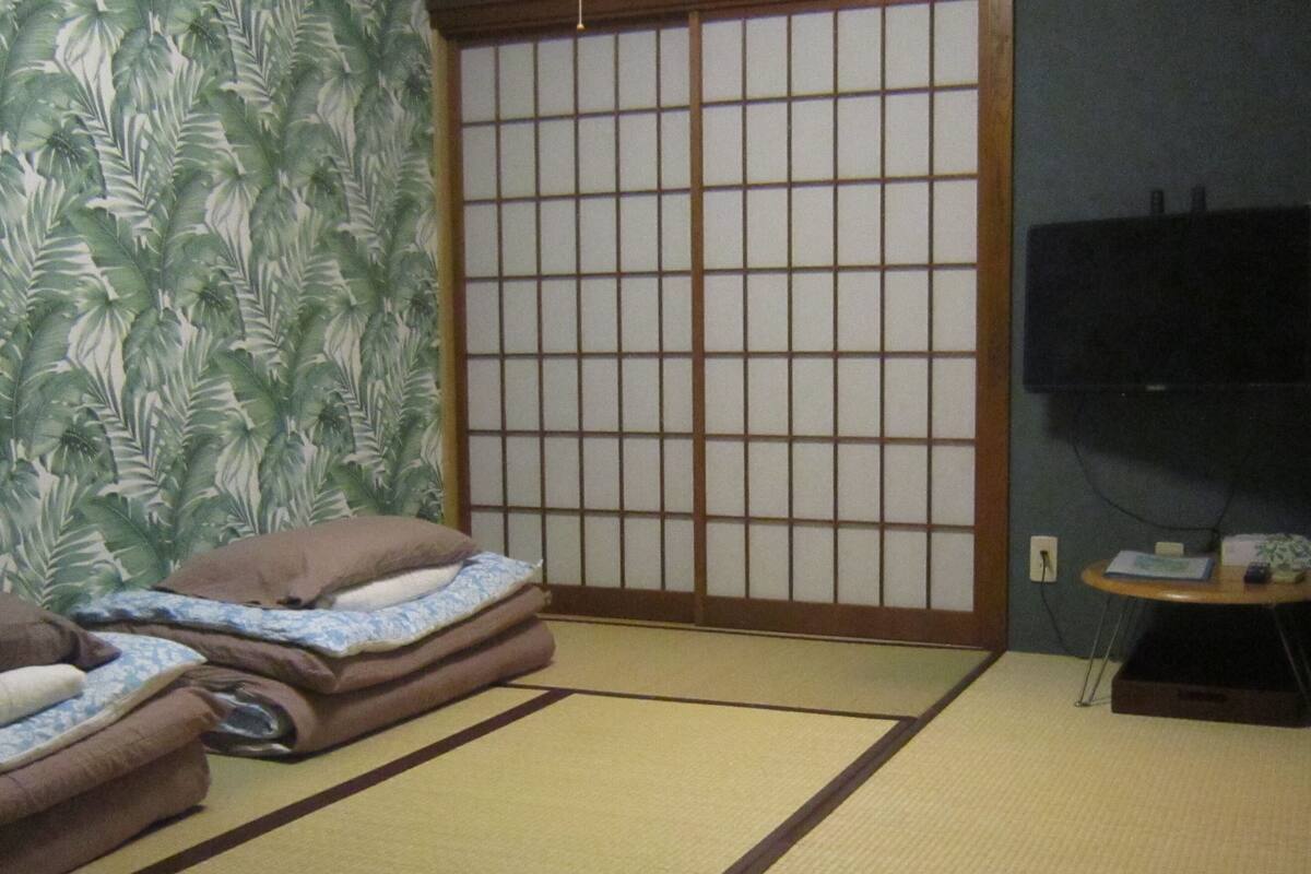 Um espaço com esteiras de tatame, um painel shoji, uma televisão e uma pequena mesa com um controle remoto.