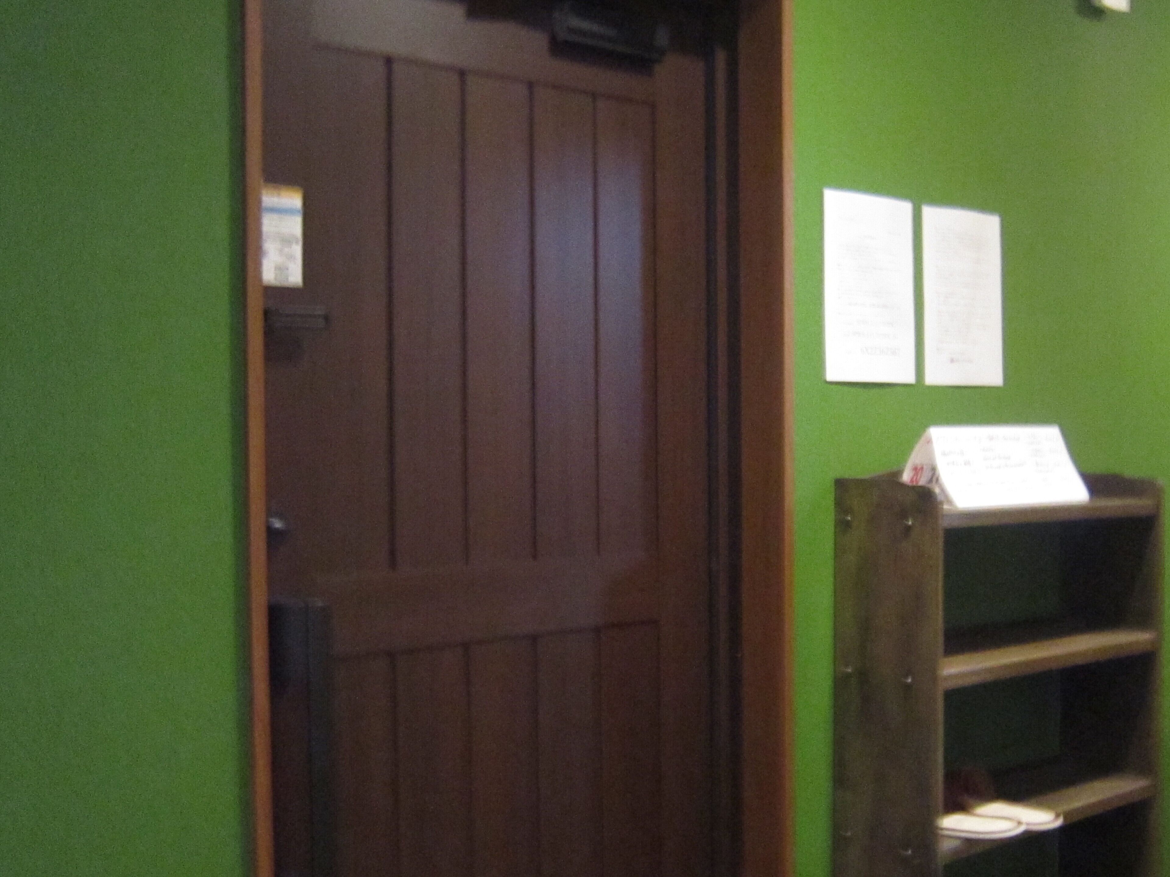 A wooden door with a dark finish, a green wall with two white papers attached, and a wooden shelf with a sign on it.