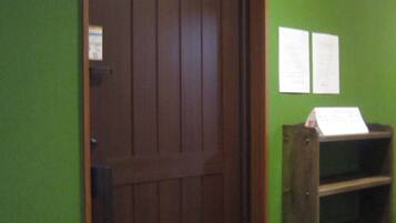 A wooden door with a dark finish, a green wall with two white papers attached, and a wooden shelf with a sign on it.