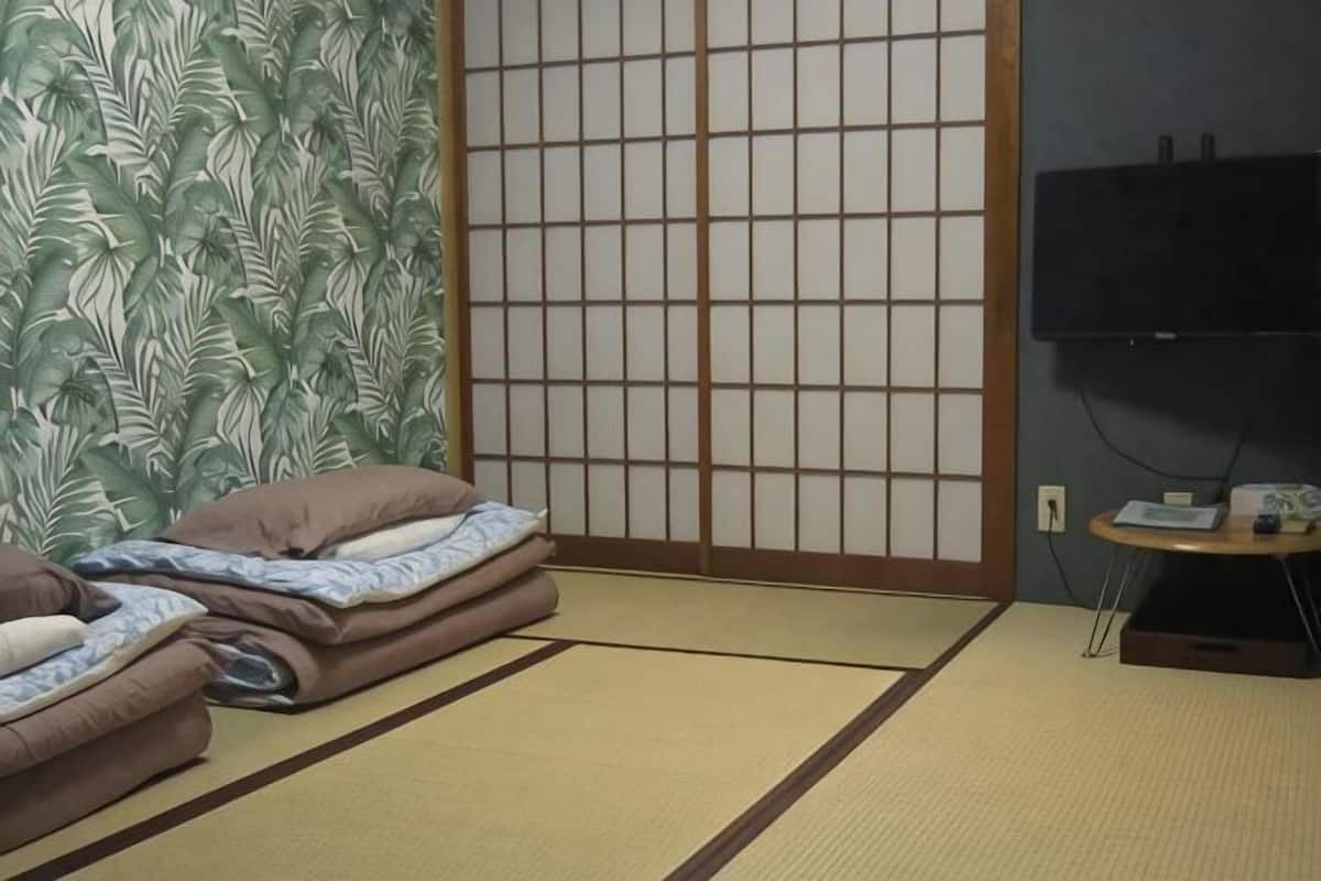 Um quarto com esteiras de tatame, uma porta deslizante, uma televisão e uma pequena mesa com controle remoto.