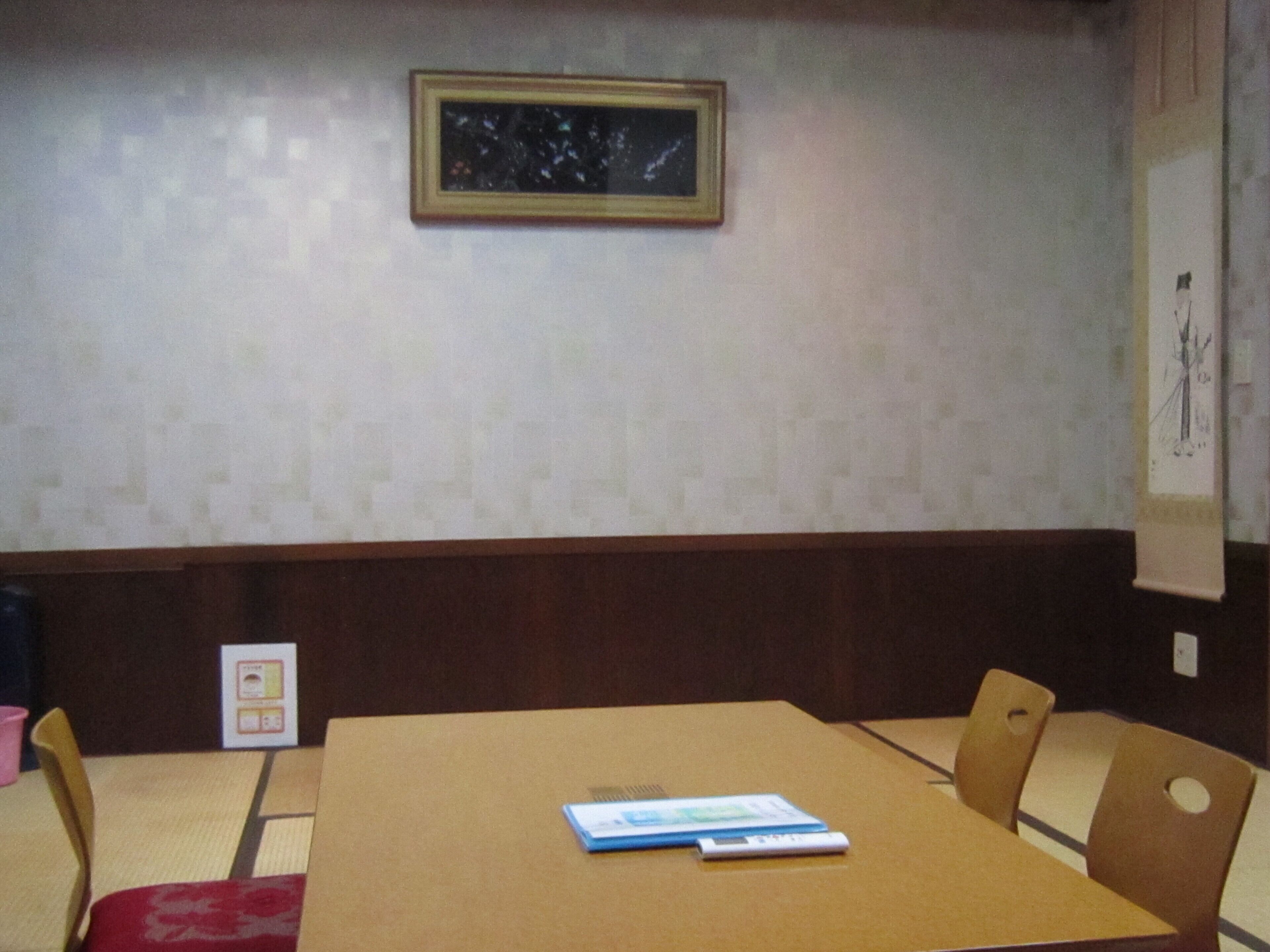 Un salón de conferencias con una mesa marrón, cuatro sillas, un cuadro en la pared y un cartel a la derecha.