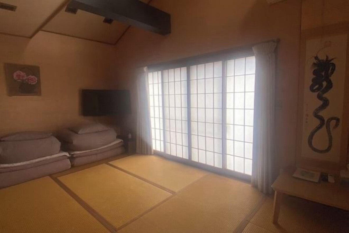A traditional Japanese room with tatami mats, a low table, a sofa, and a sliding door with a view.