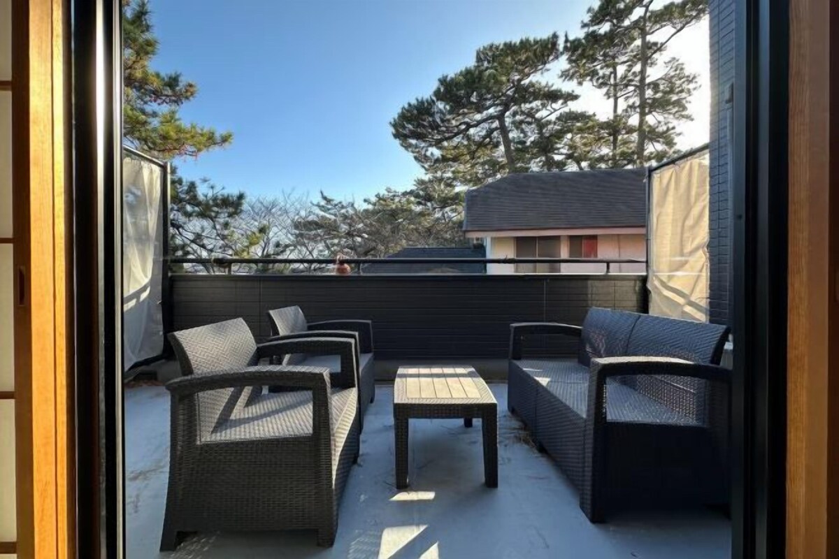 An outdoor balcony with wicker furniture, a small table, and a view of trees and buildings.