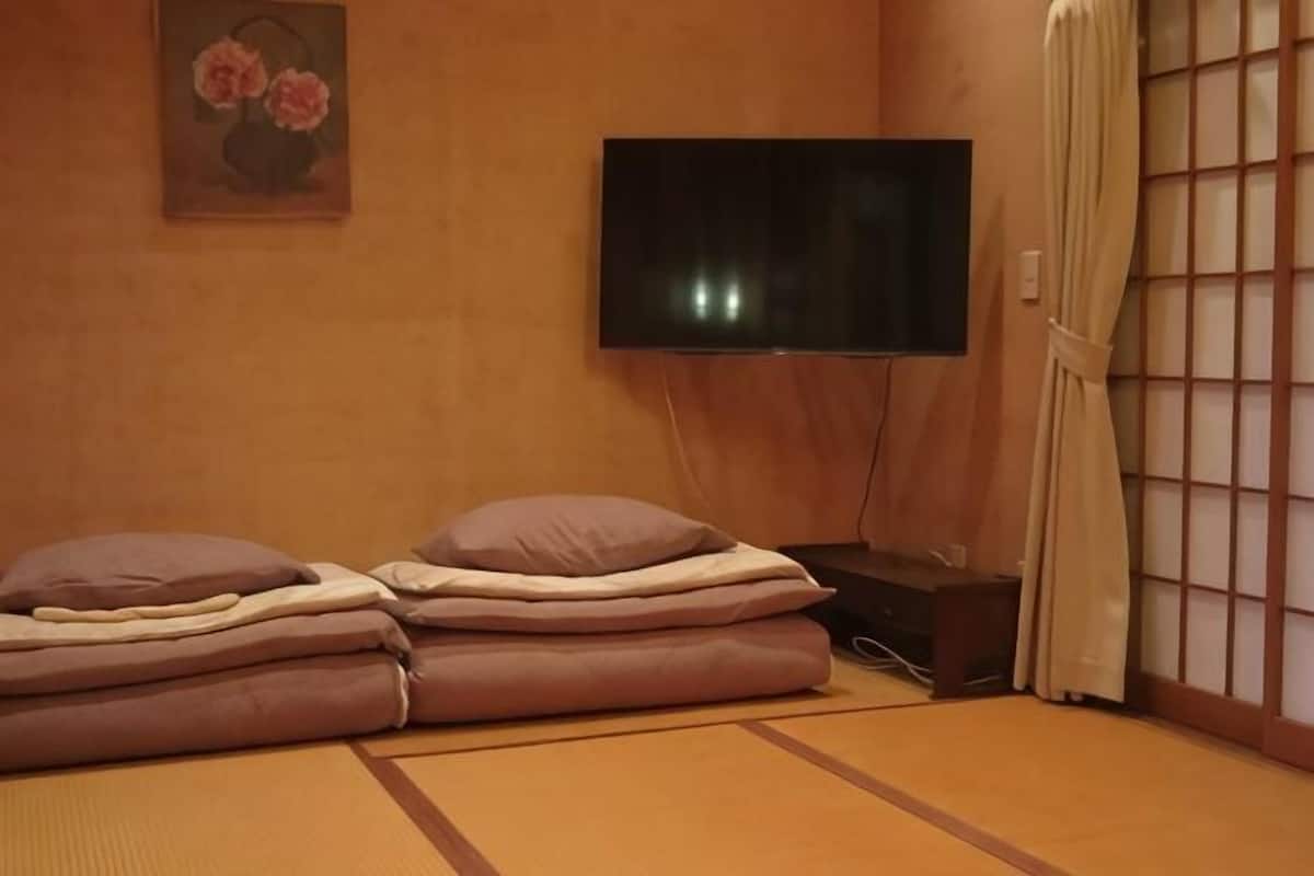 Quarto com piso de tatame, televisão, cama futon e porta corrediça tradicional.