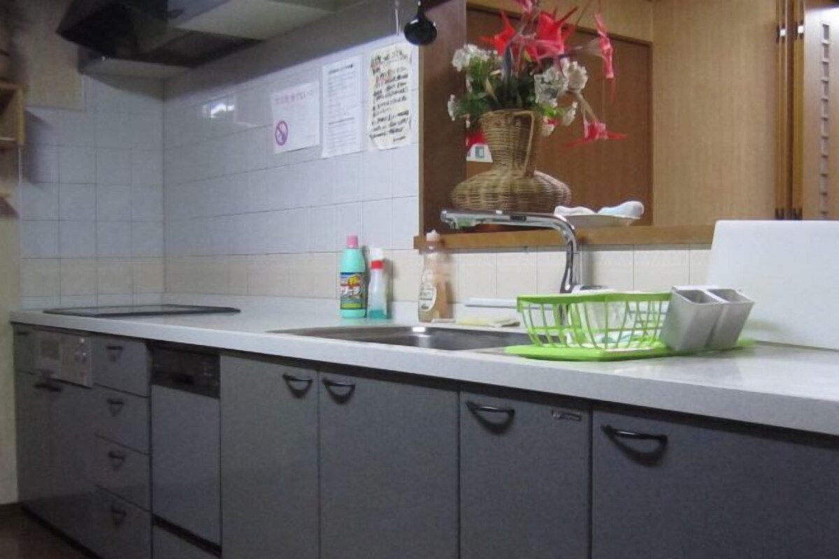 A kitchen with a white countertop, a sink, a green dish rack, and cabinets.
