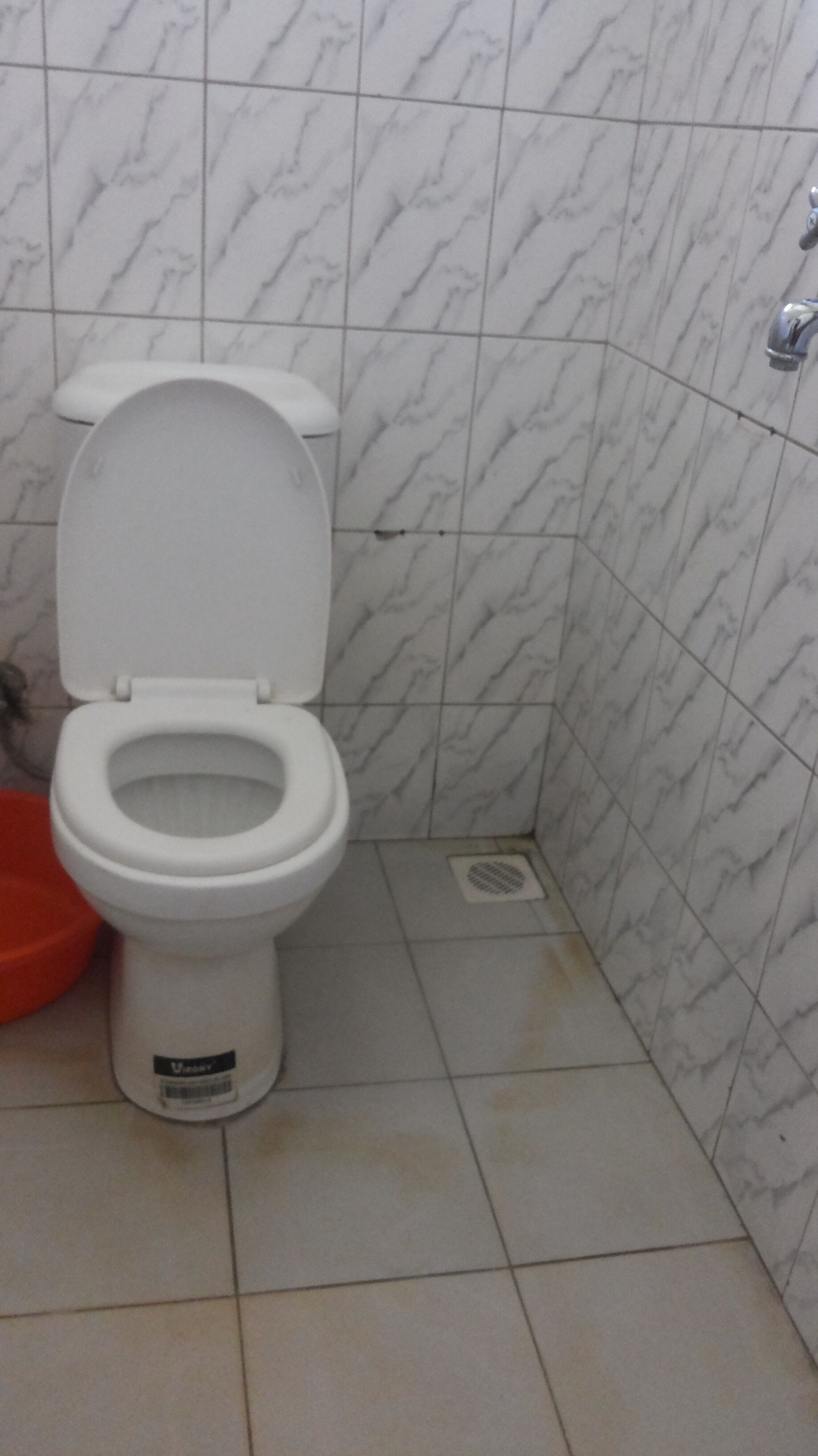Un baño con inodoro blanco, lavamanos rojo y paredes con diseño de mármol.