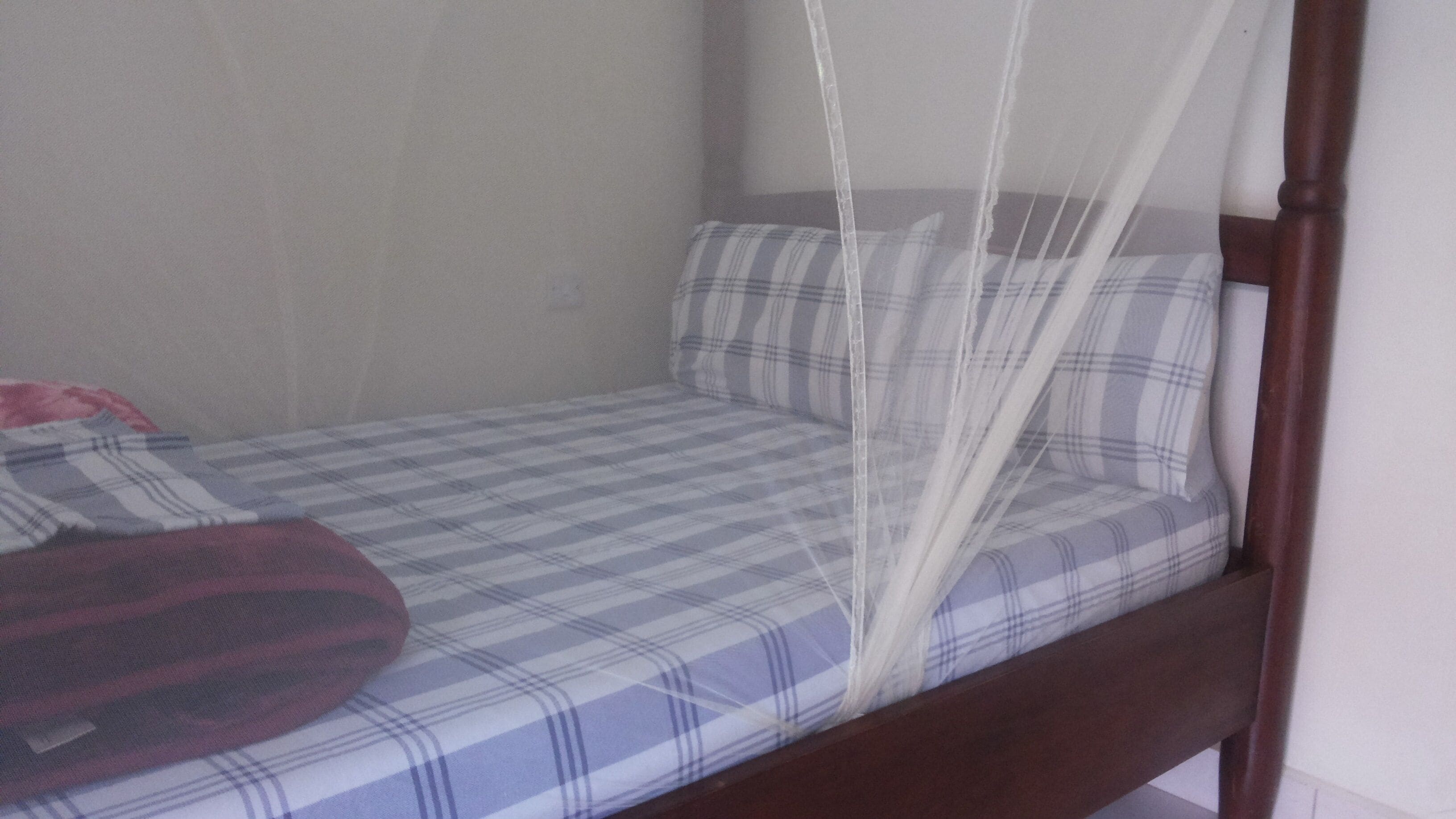 A single bed with a plaid bedspread and a mosquito net.