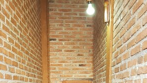 Un couloir étroit aux murs de briques, avec une porte en bois et un luminaire fixé au mur.