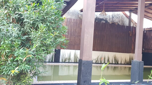 Un espace extérieur abrité, doté d’une clôture en bois, d’un luminaire suspendu et d’un élément décoratif aquatique.