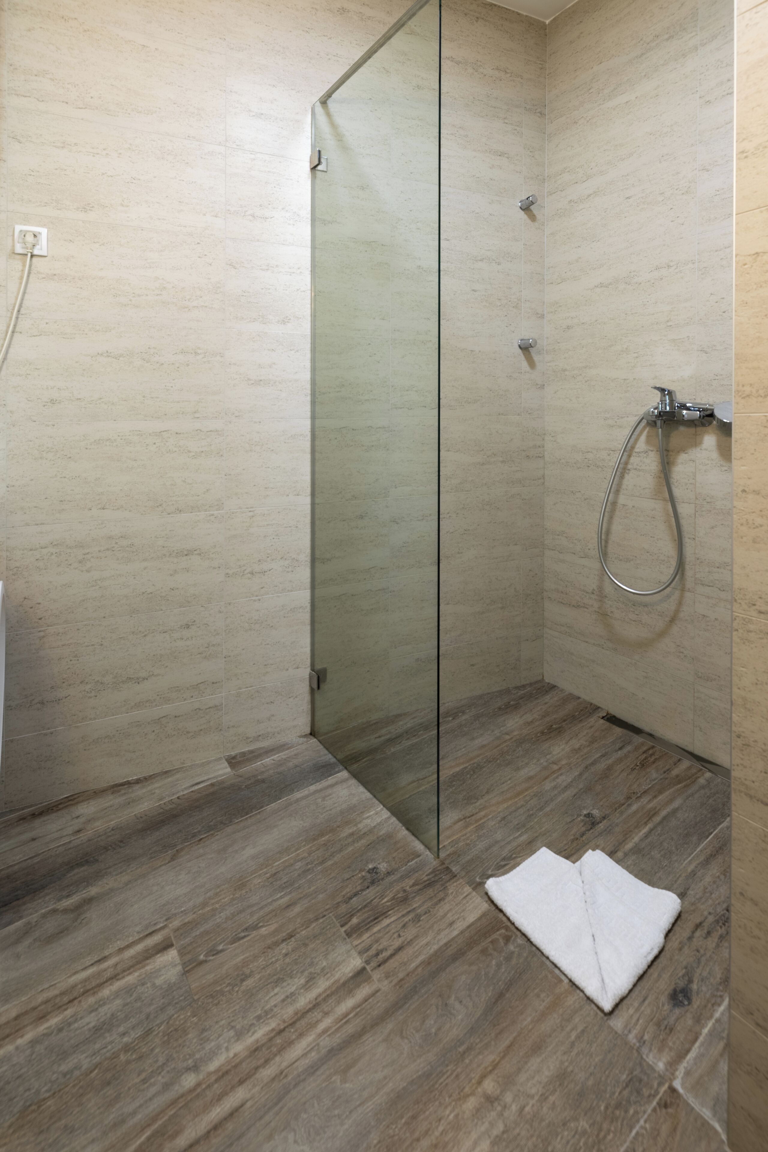 Ein modernes Badezimmer mit Duschkabine aus Glas, Holzboden und einem weißen Handtuch auf dem Boden.