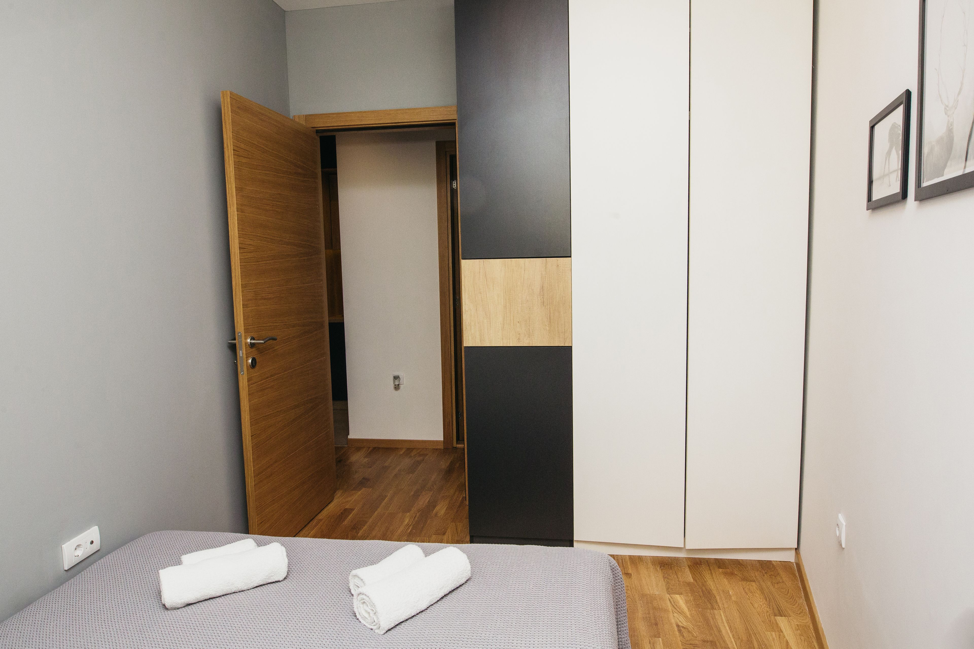 A bedroom with a bed, a wooden wardrobe, and a door leading to another room.