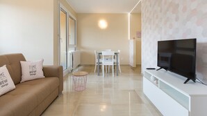 A modern living room with a sofa, a TV on a stand, a dining table with chairs, and a patterned wall. - Pazzallo Apartments (Lugano)