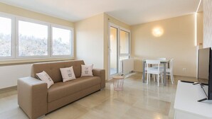 A modern living room with a beige sofa, a dining table with chairs, and a TV. - Pazzallo Apartments (Lugano)