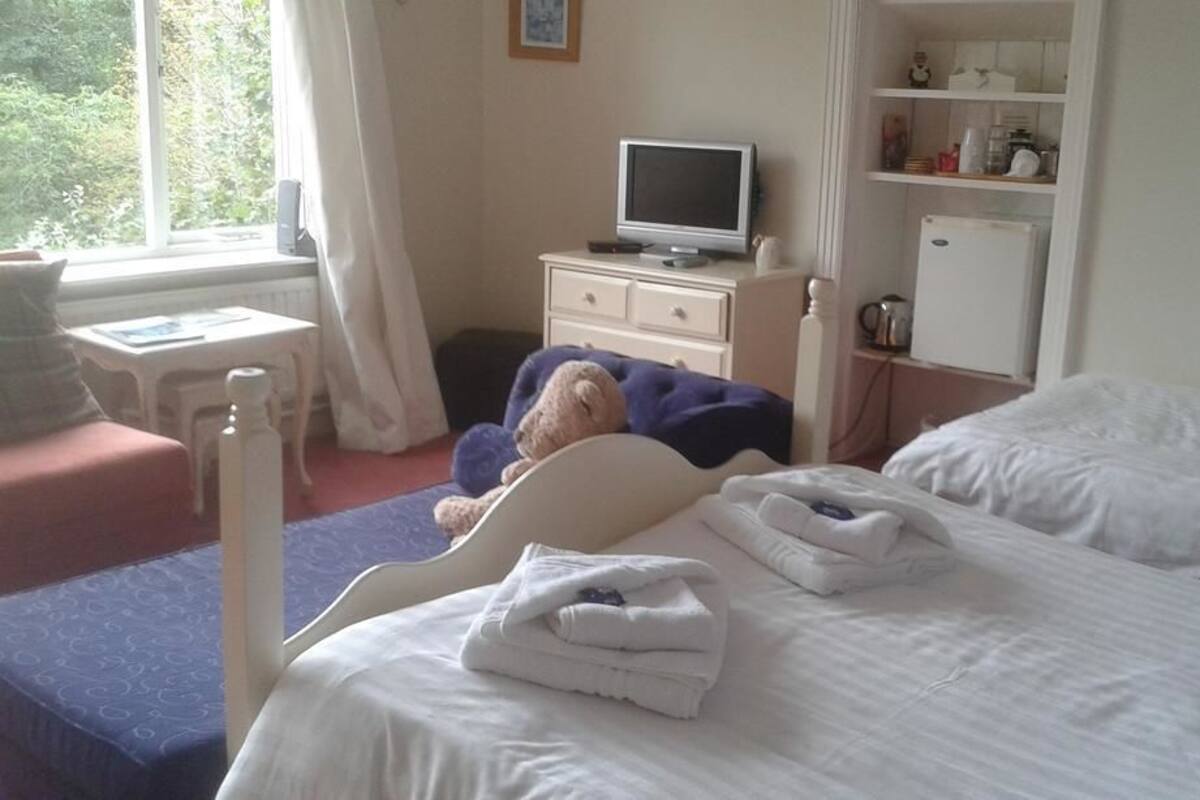 A hotel room with a bed, a bedside table, a television, and a small kitchenette.