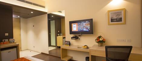 A hotel room with a bed, desk, chair, television, and a small kitchenette.