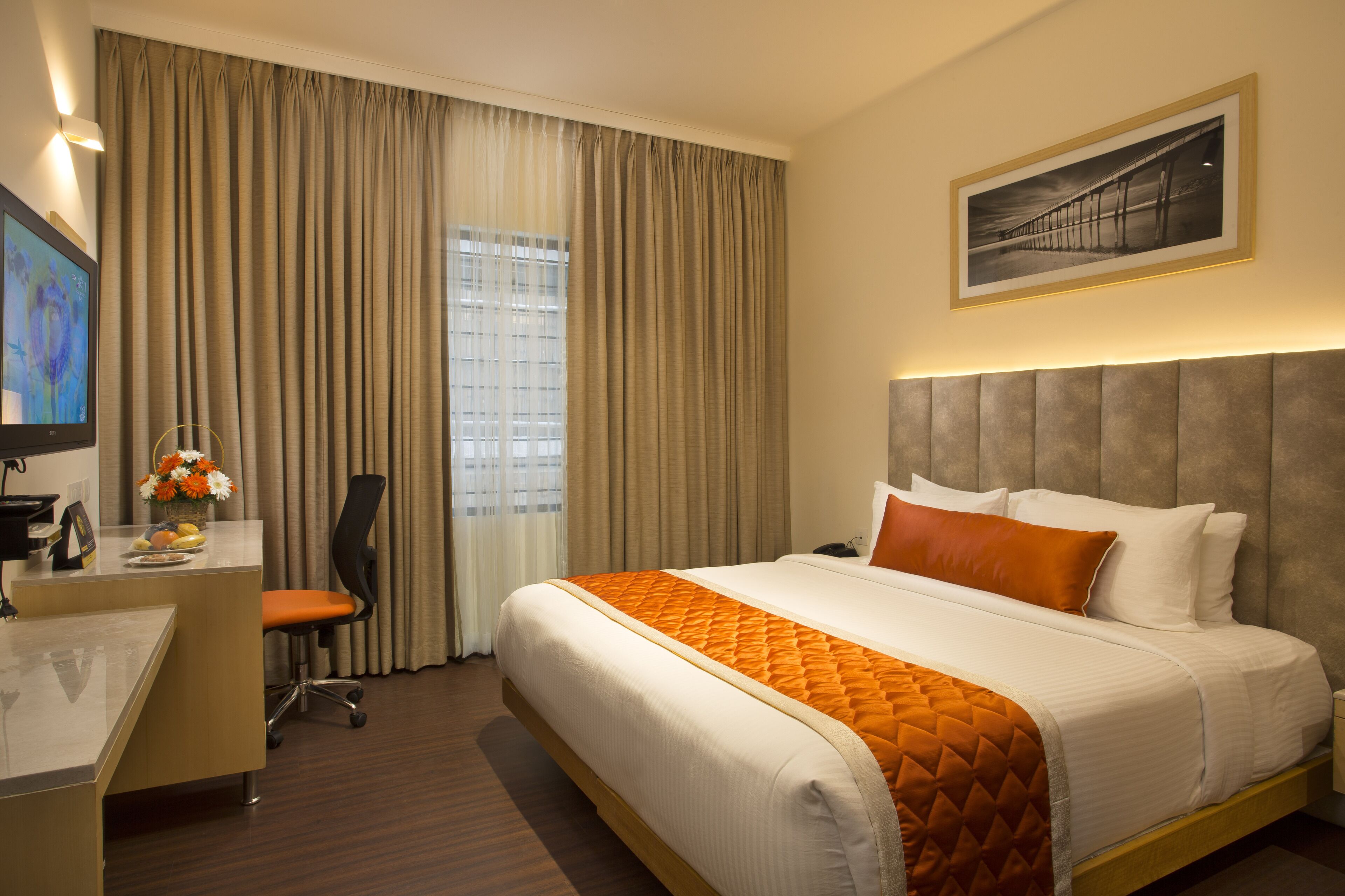 A hotel room with a large bed, a desk with a chair, a television, and a framed picture on the wall.