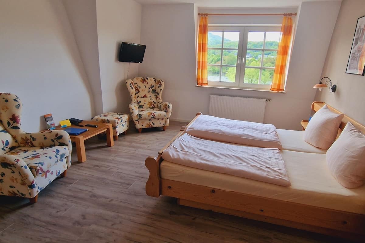 A room with a bed, two armchairs, a small table, a TV, and a window with curtains.