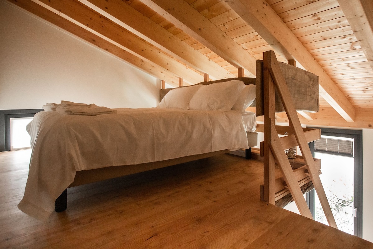 Ein Schlafzimmer im Loft-Stil mit Holzbalkendecke, einem Bett und einer Leiter.