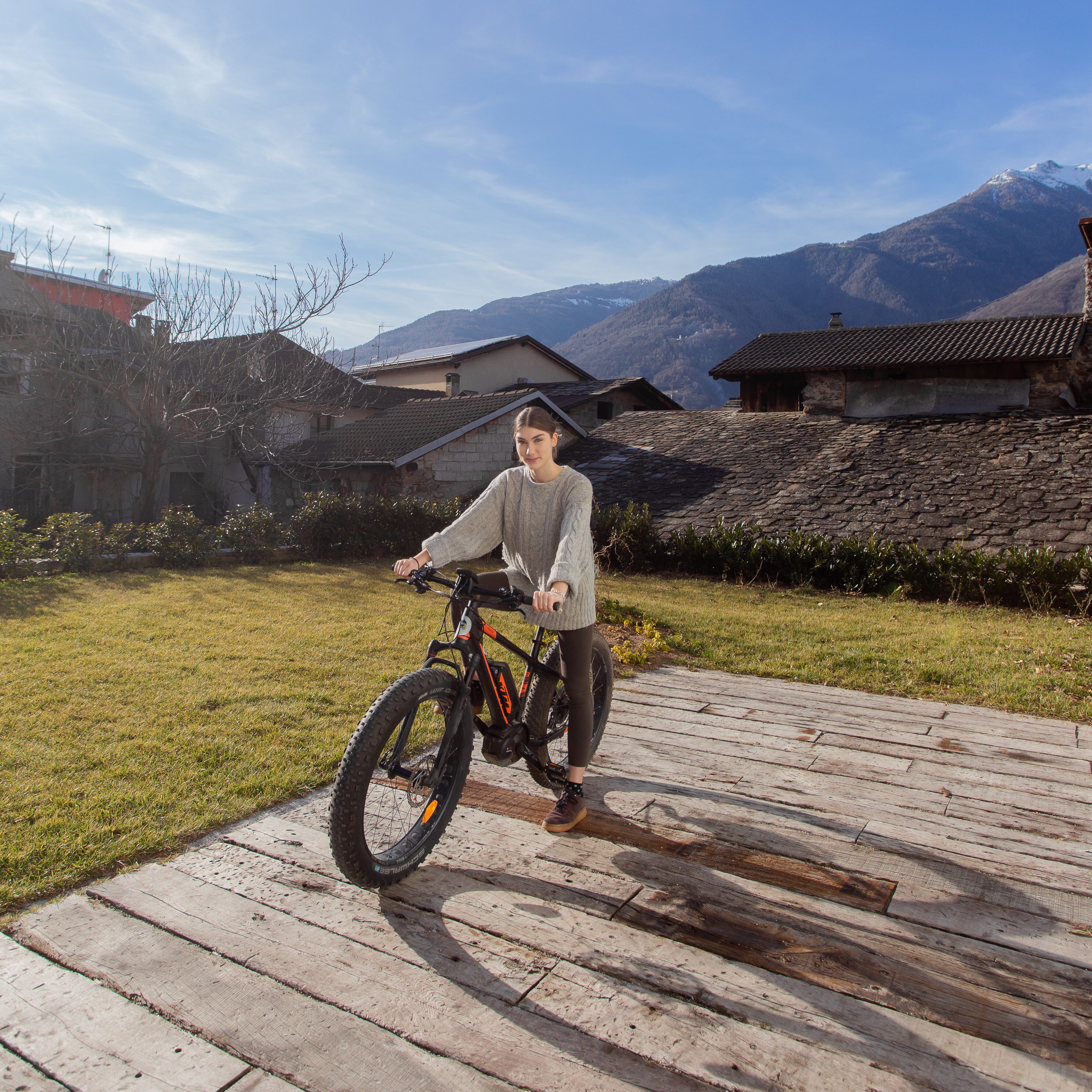 Una persona montando en bicicleta sobre una terraza de madera con montañas al fondo.