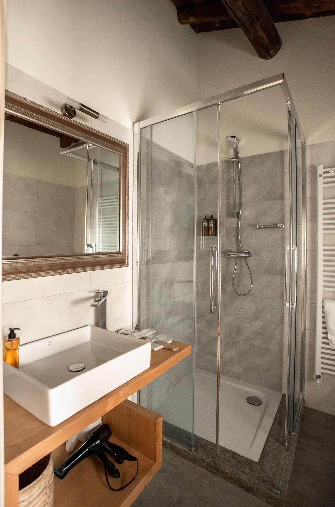 Een moderne badkamer met een douchecabine van glas, een witte wastafel met houten opbergruimte en een grote spiegel erboven.