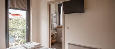 A bedroom with a bed, a radiator, a TV mounted on the wall, and a view of the outside balcony.