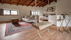 Un vaste salon doté d’un plafond en bois, d’une balançoire, d’un canapé, d’un lit et d’une petite table sur laquelle se trouvent une bouteille et des verres.