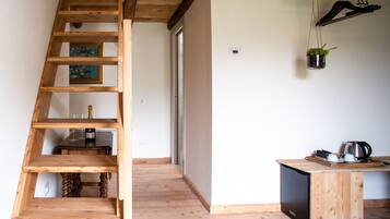 Una escalera de madera que lleva a un cuarto con un escritorio, una planta colgante y una puerta al fondo.