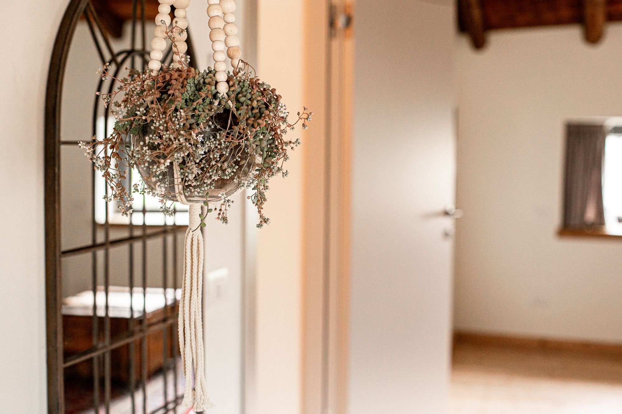 A hanging wooden ornament with dried flowers and greenery, a metal railing, and a wooden door in a room with white walls.