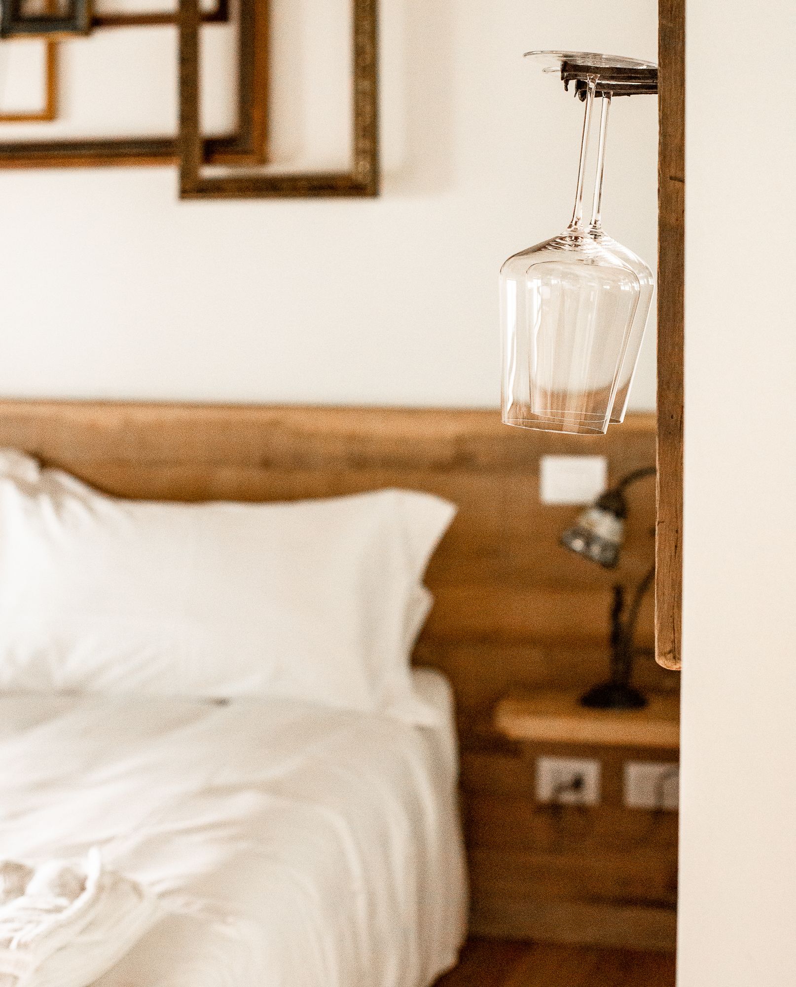 Une chambre à coucher avec une tête de lit en bois, une couvre-lit blanche et une bouteille en verre transparent suspendue au plafond.