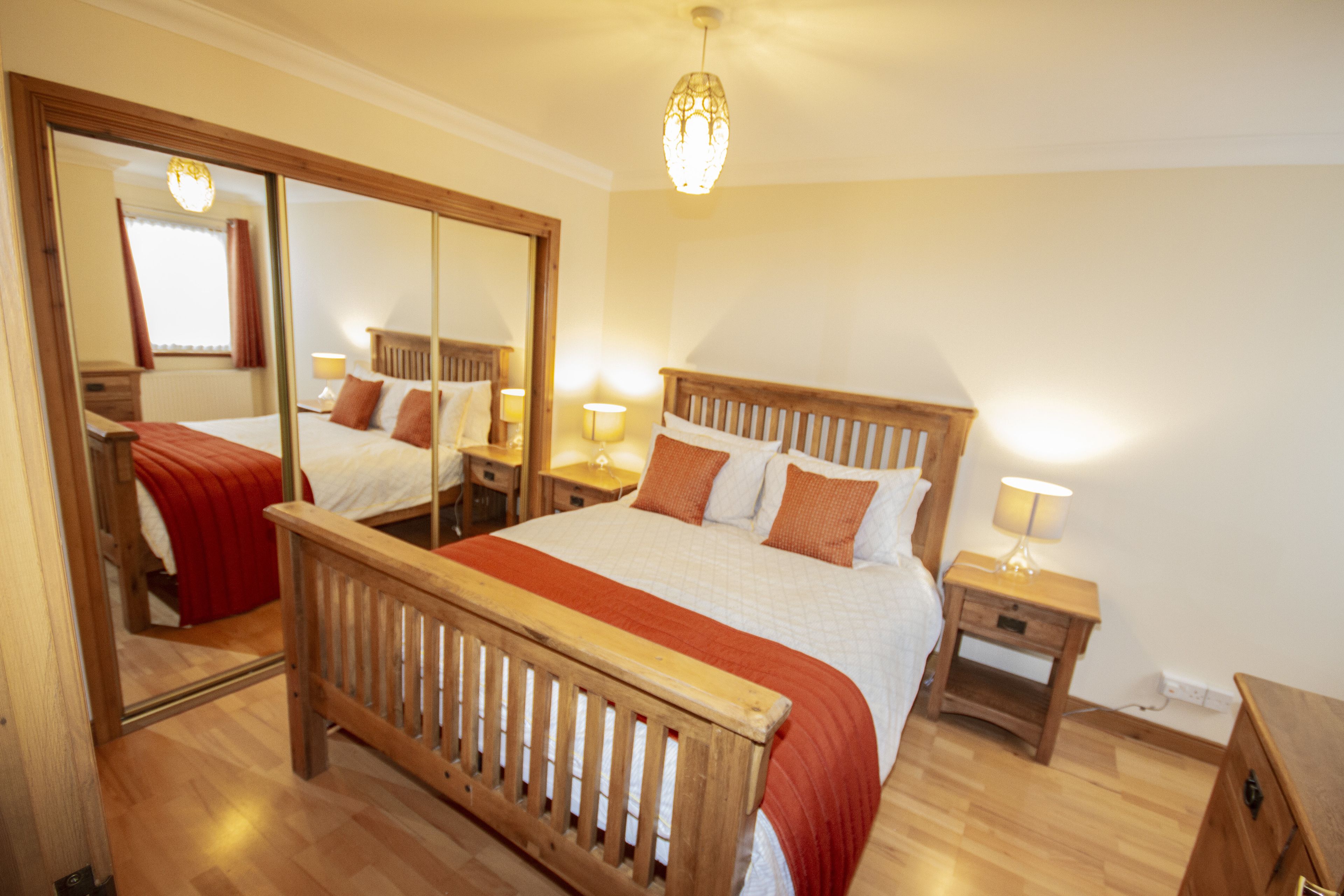 A bedroom with a wooden bed, a nightstand with a lamp, a mirror, and a chandelier.