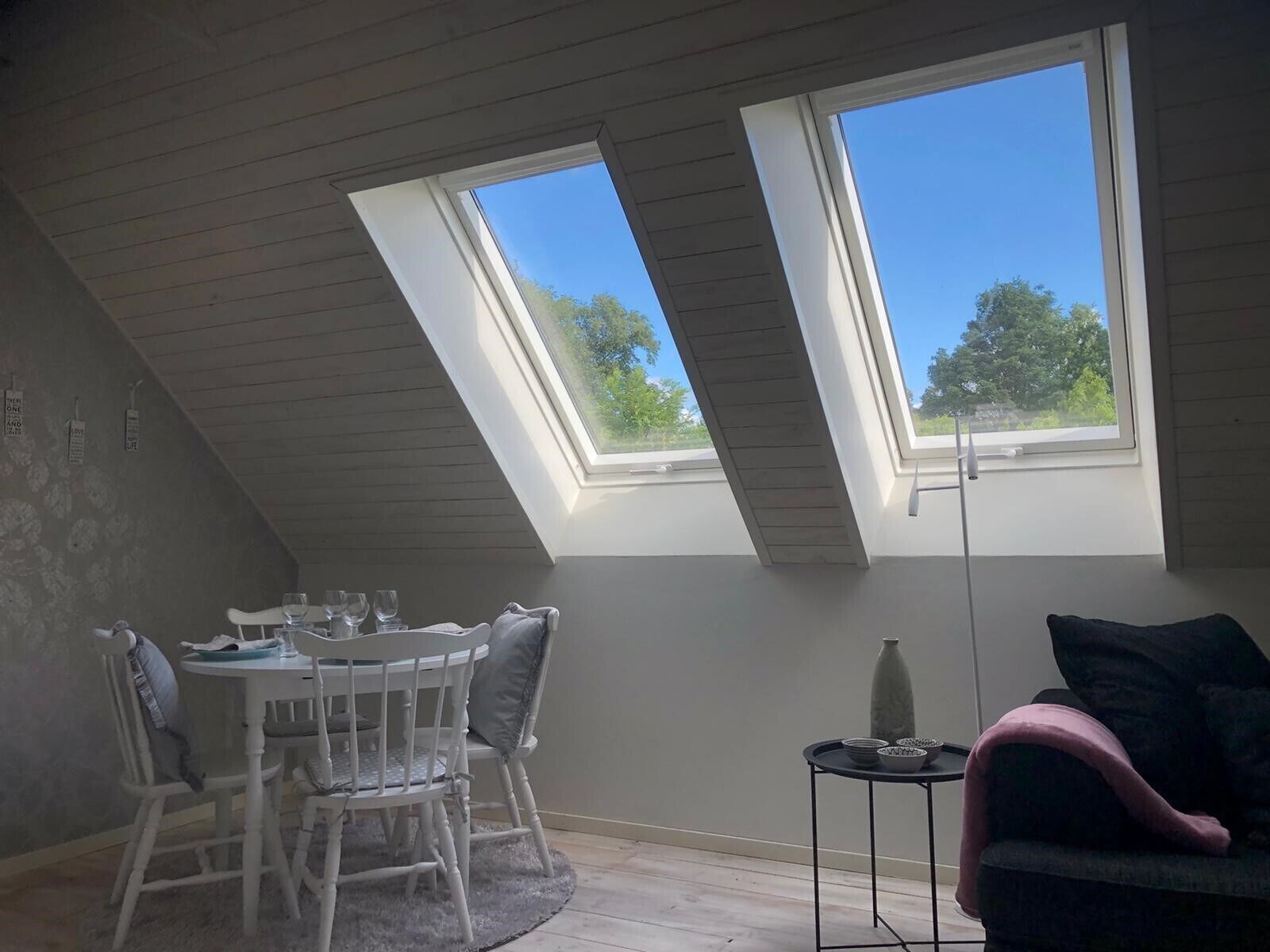 Une pièce avec un plafond en pente, deux fenêtres de toit, une table à manger avec des chaises, une petite table d’appoint et un canapé.