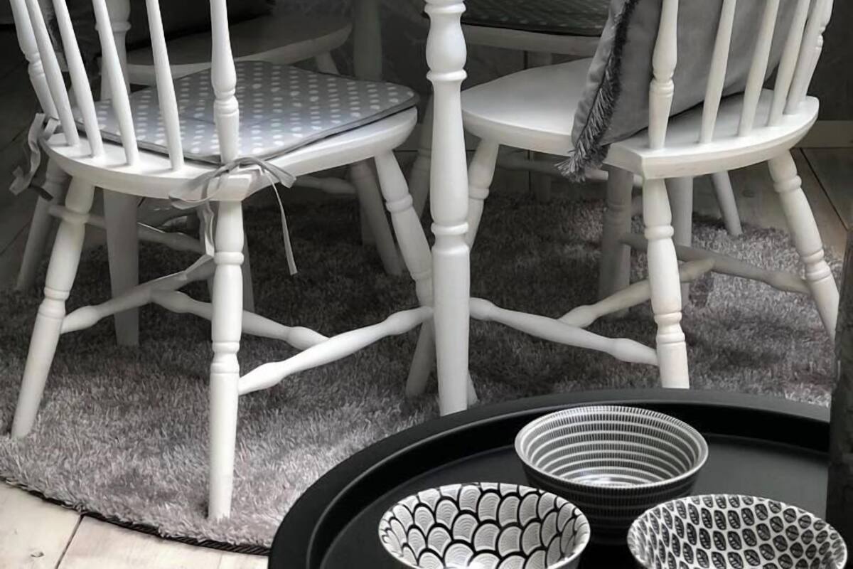 A round dining table with white chairs, set with plates, glasses, and a napkin.