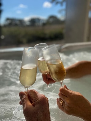 Two hands holding champagne glasses over a hot tub. - Lugna Gården- Spa & Konferens (Löberöd)