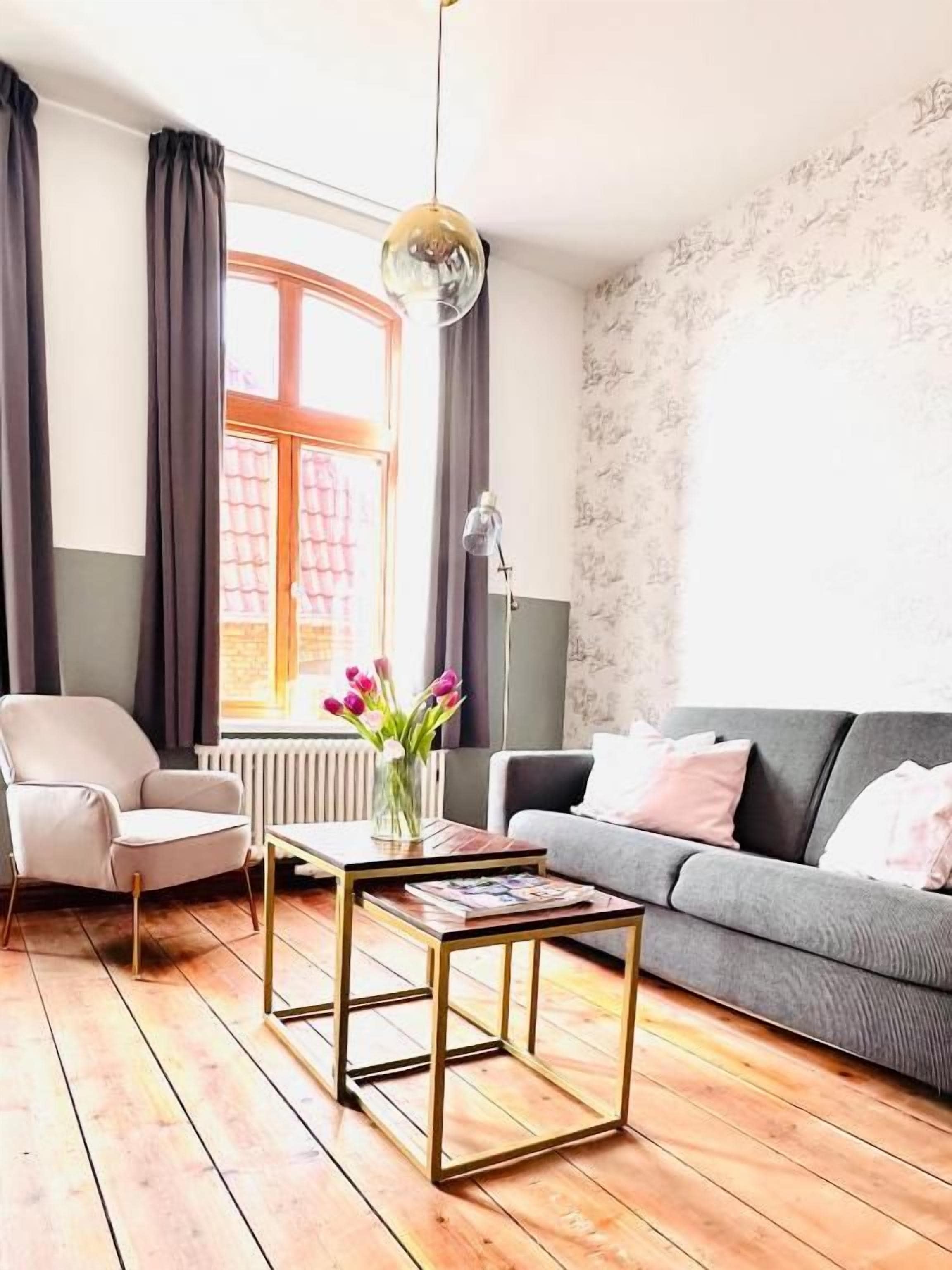 A living room with a sofa, armchair, coffee table, and a window with curtains.