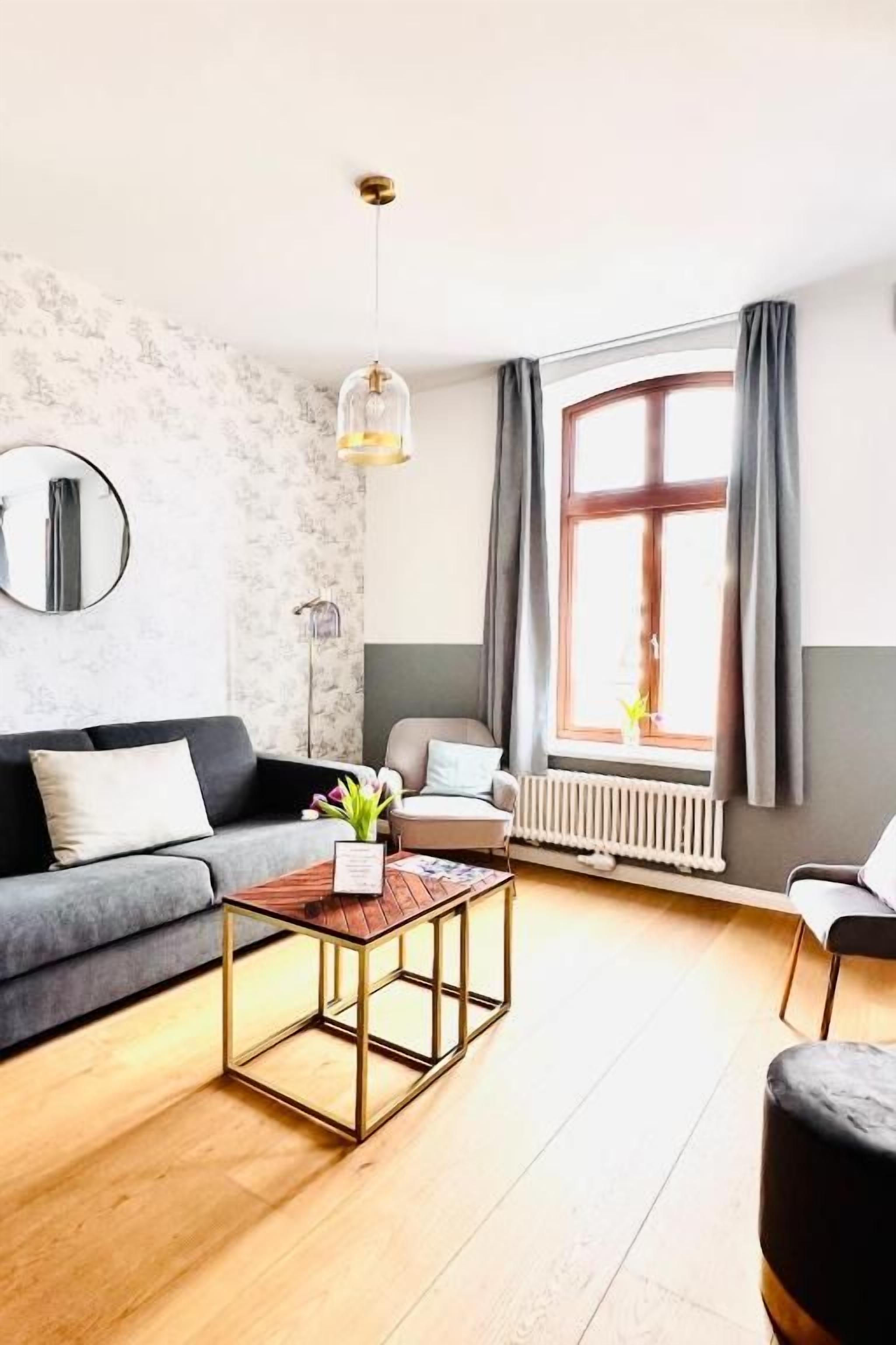 Una sala de estar moderna con un sofá, una mesa de centro, una silla y un ventanal con cortinas.