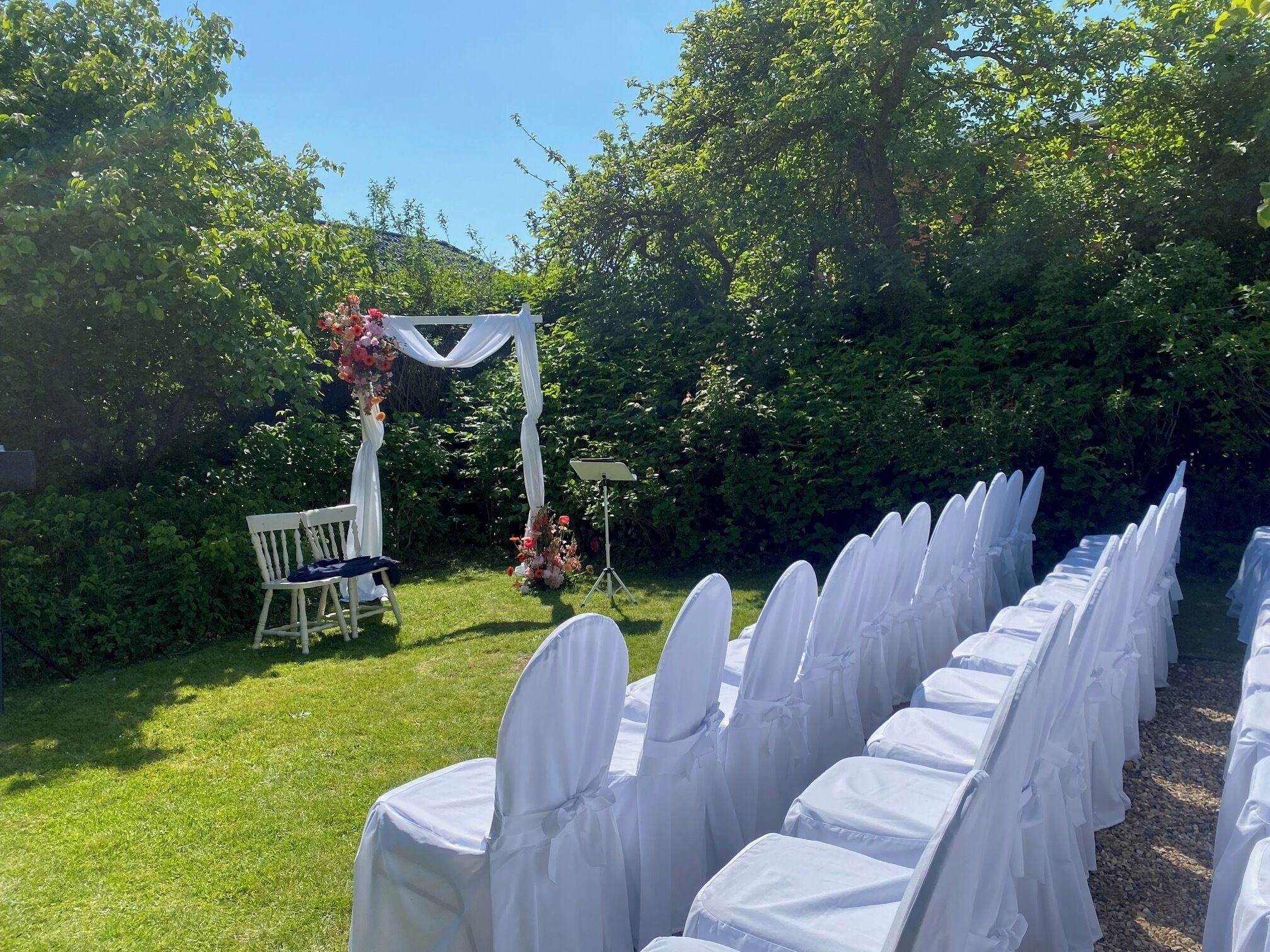 A row of white-covered chairs with a white chair and a music stand in the background.