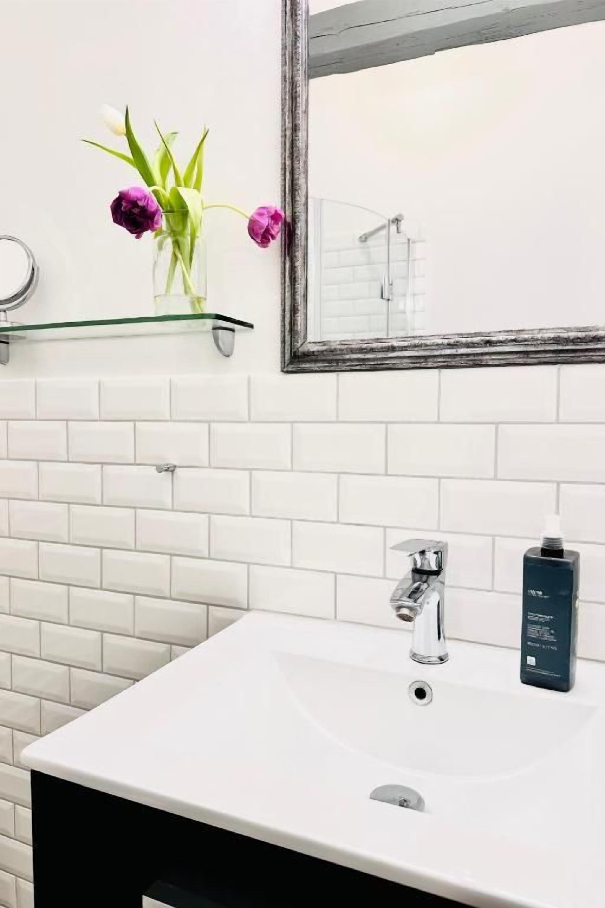 Une salle de bain avec un lavabo blanc, un miroir et une étagère en verre ornée de fleurs.
