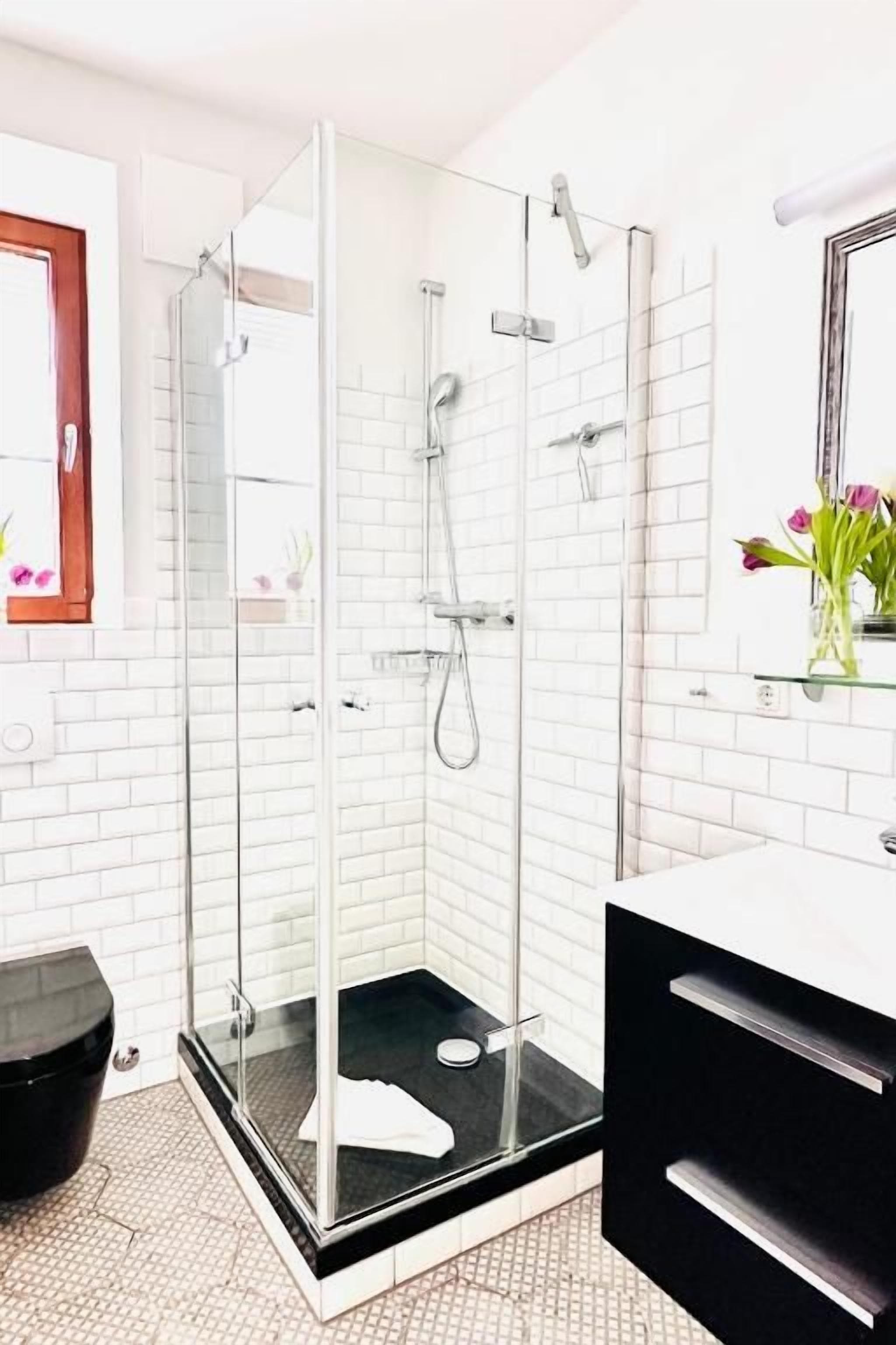 A modern bathroom with a glass-enclosed shower, white tiled walls, and a black vanity.