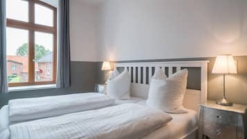 Habitació d'hotel amb dos llits, una finestra amb cortines, una tauleta de nit amb una làmpada i vista a un edifici.