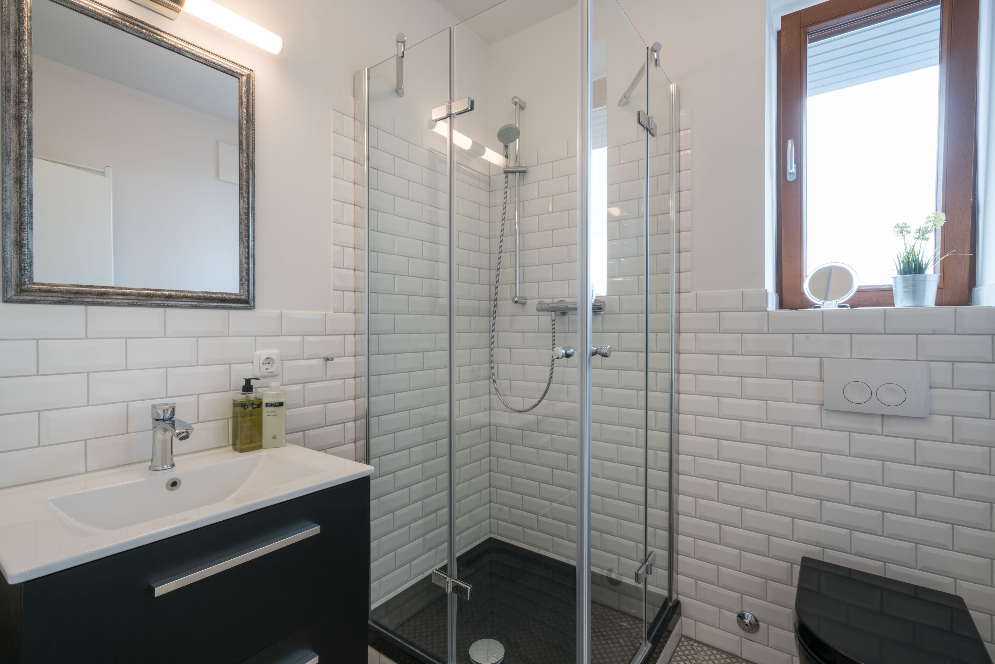 A modern bathroom with a glass-enclosed shower, white subway tiles, a black vanity, and a mirror with a gold frame.