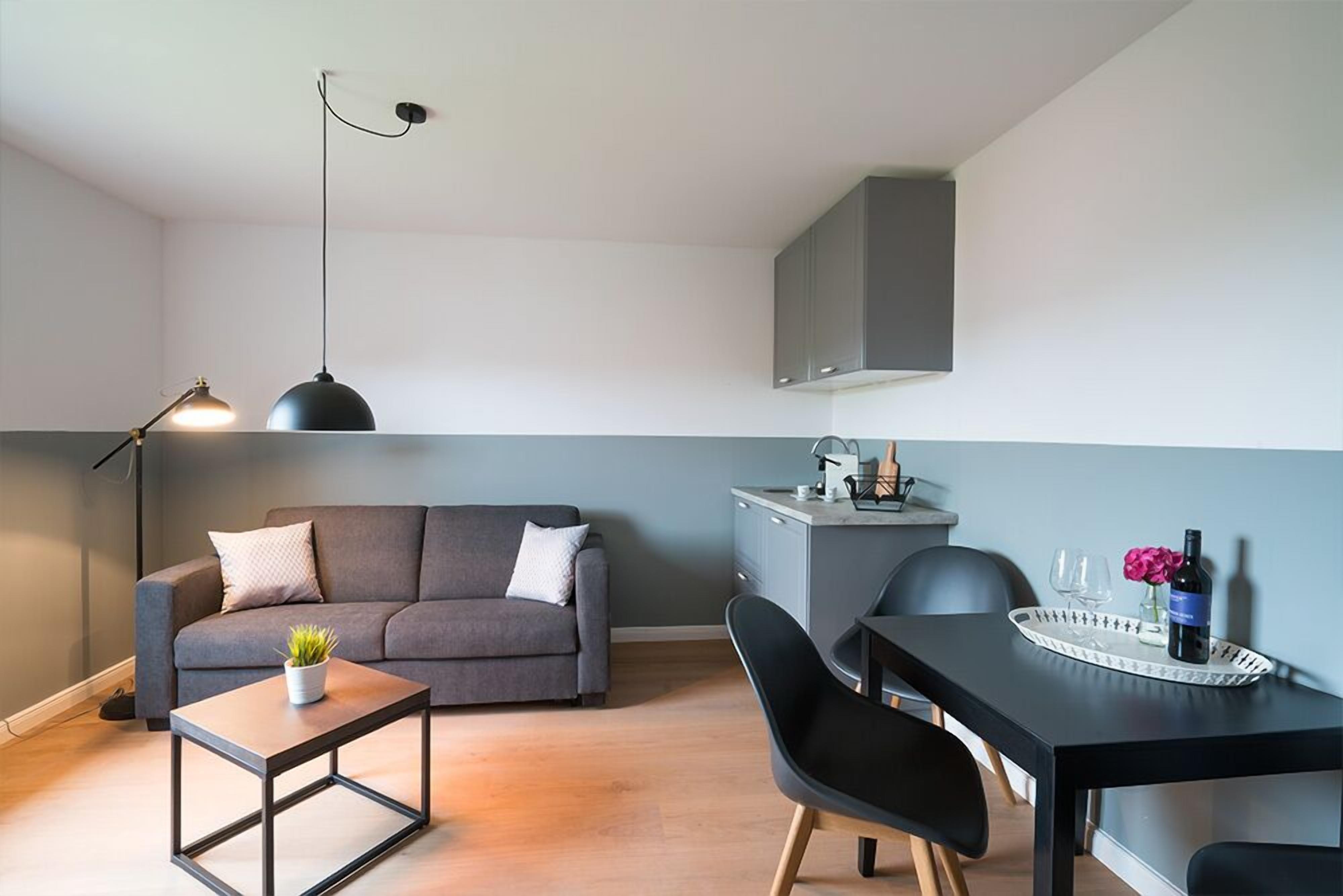 Ein modernes Wohnzimmer mit einer Couch, einem Couchtisch, einem Esstisch mit Stühlen, einer Pendelleuchte und einer Küchenzeile.