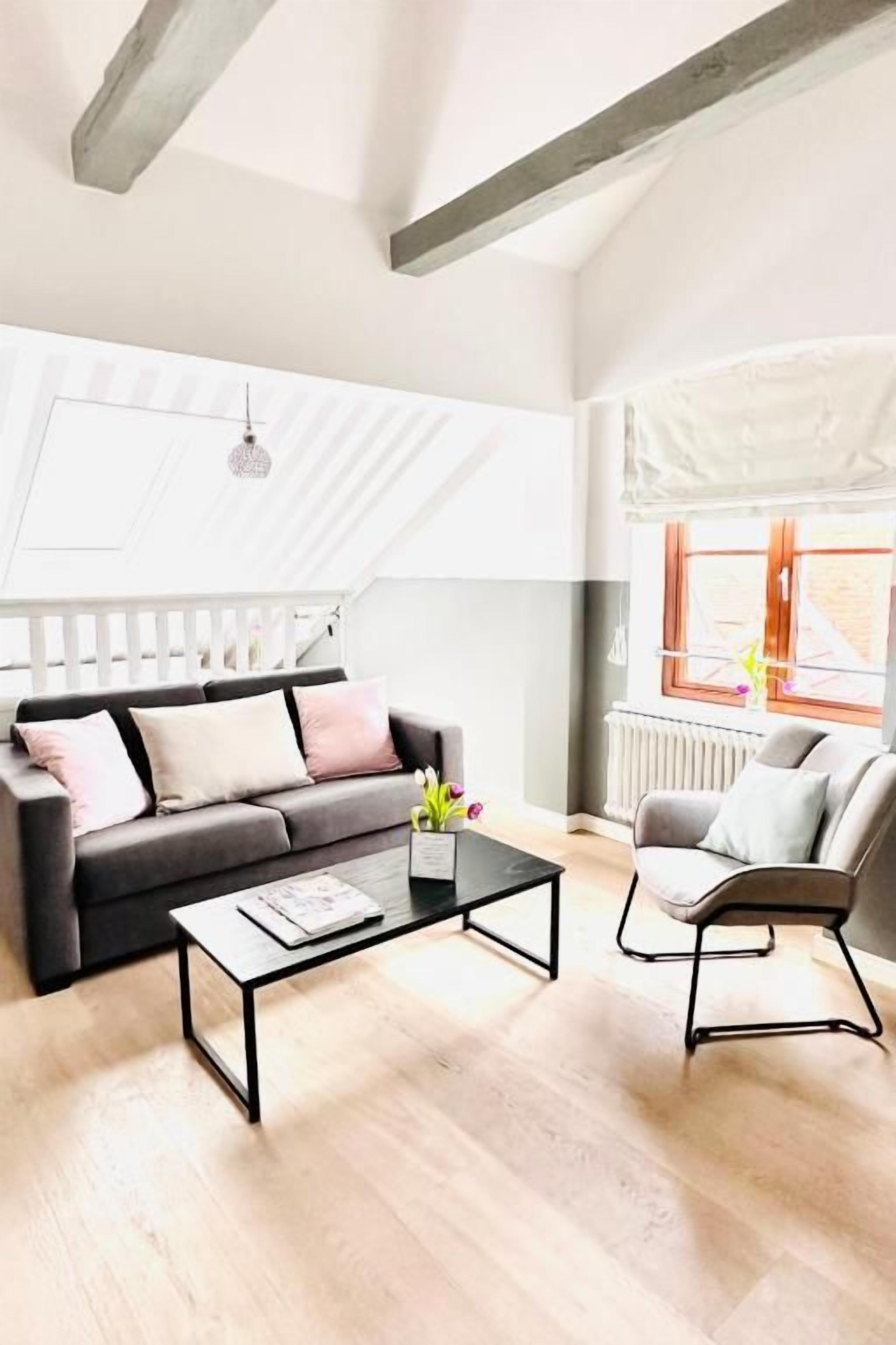 Ein Wohnzimmer mit einer Couch, einem Couchtisch und einem Sessel. Ein Fenster bietet Blick ins Freie.