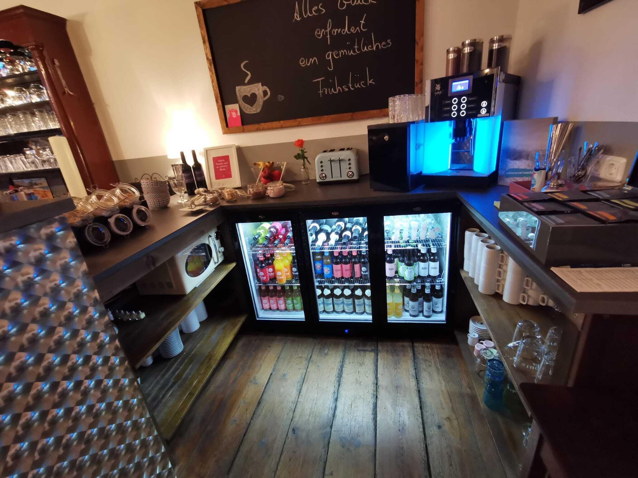 A bar area with a chalkboard displaying a message, a coffee machine, and multiple refrigerators stocked with beverages.