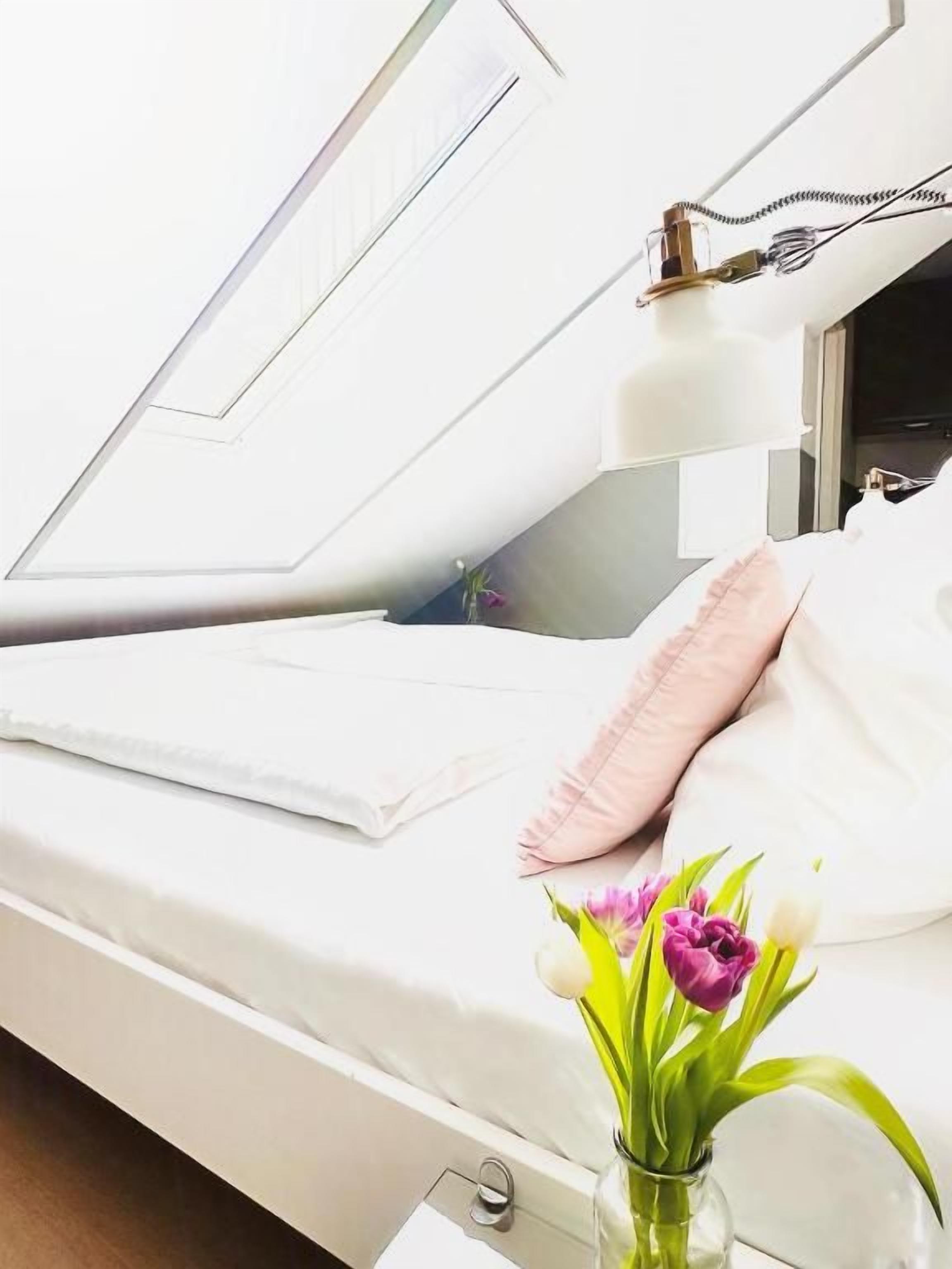 A hospital room with a bed, a bedside table with a vase of flowers, and a window with blinds.