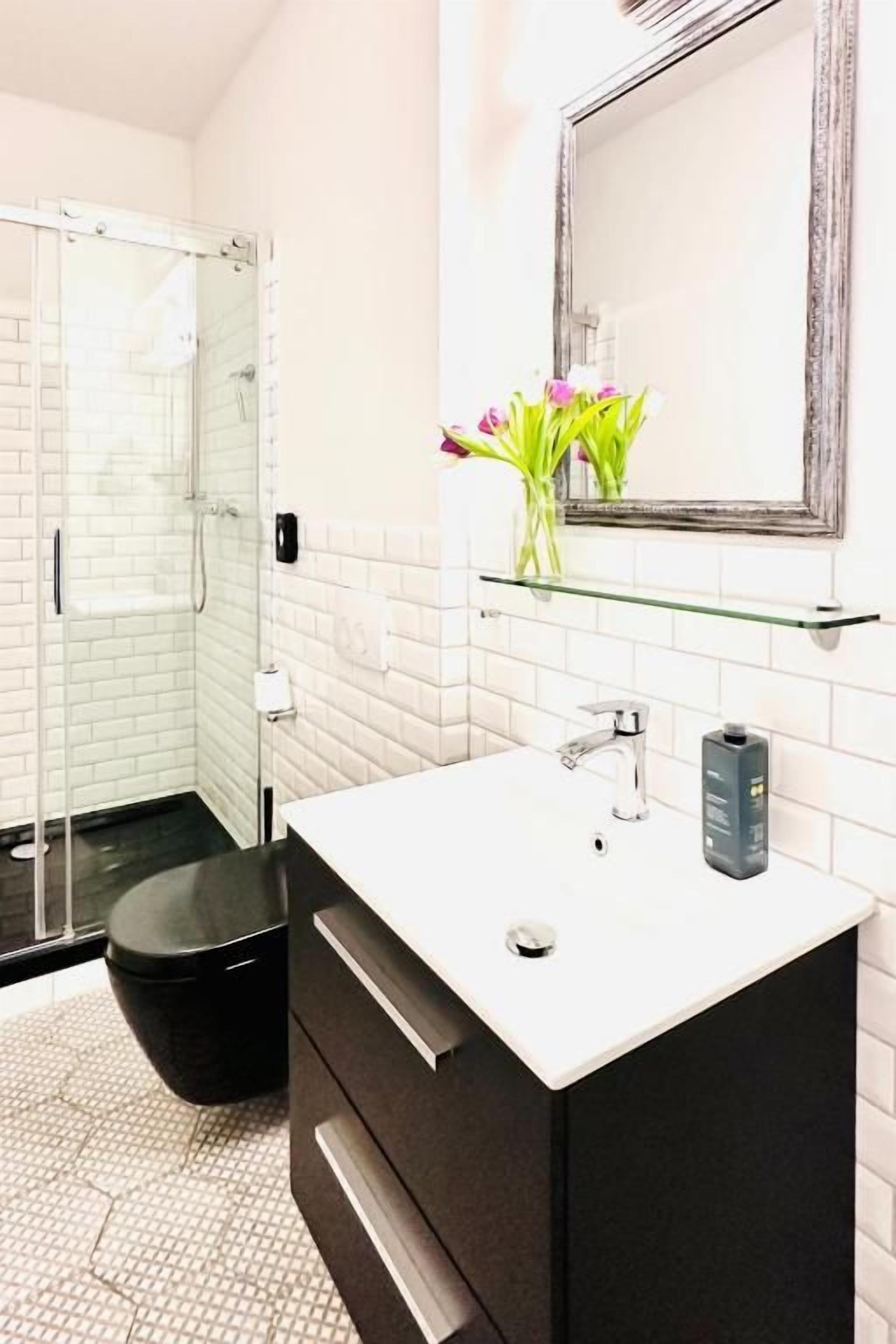 A bathroom with a glass shower enclosure, a white sink with a black cabinet, and a mirror above the sink.