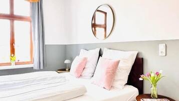 Un dormitorio con cama, mesita de noche, espejo y ventana con cortinas.