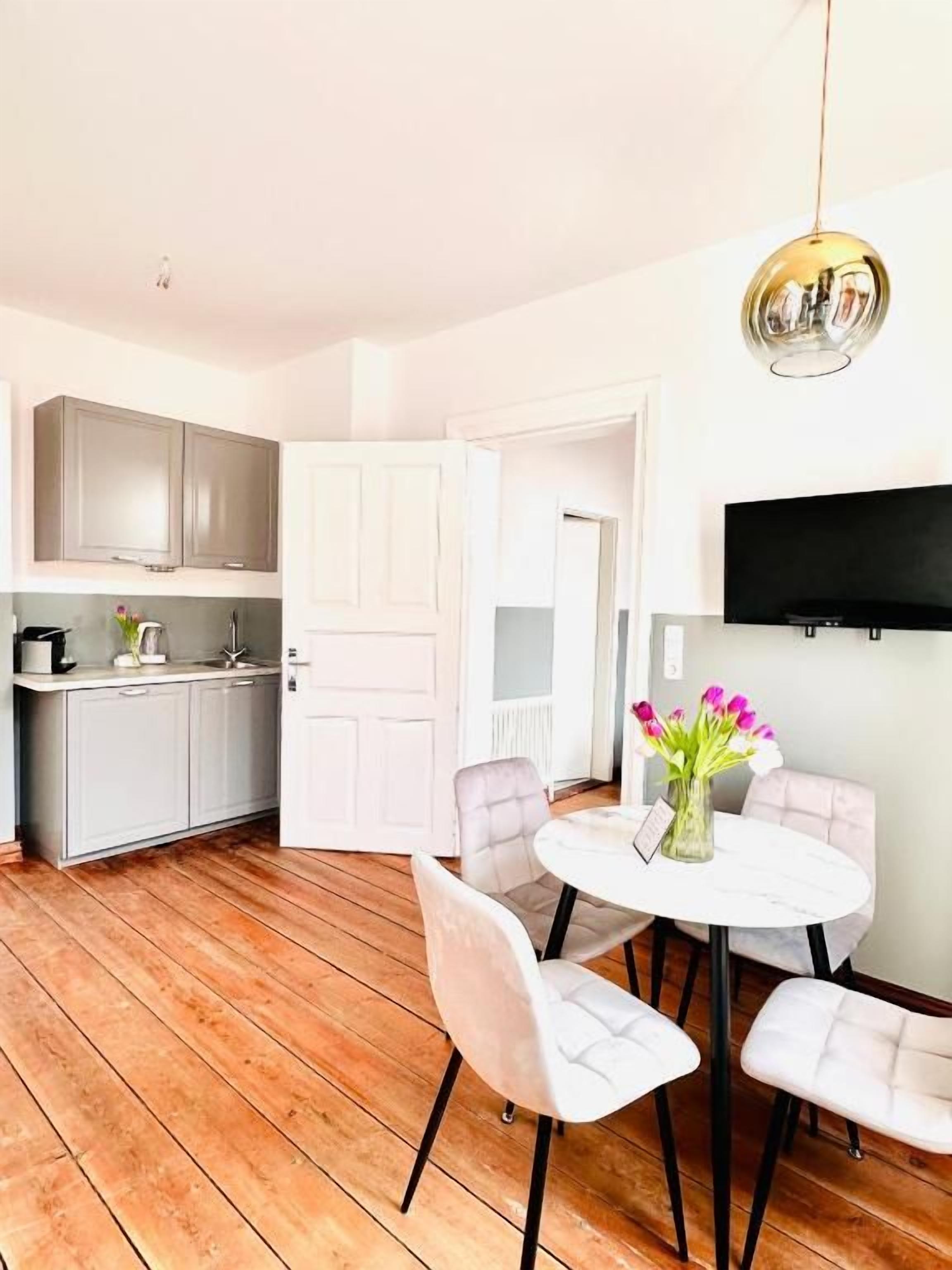 Une cuisine moderne avec des meubles gris, un plan de travail blanc et un coin repas comprenant une table et des chaises blanches.