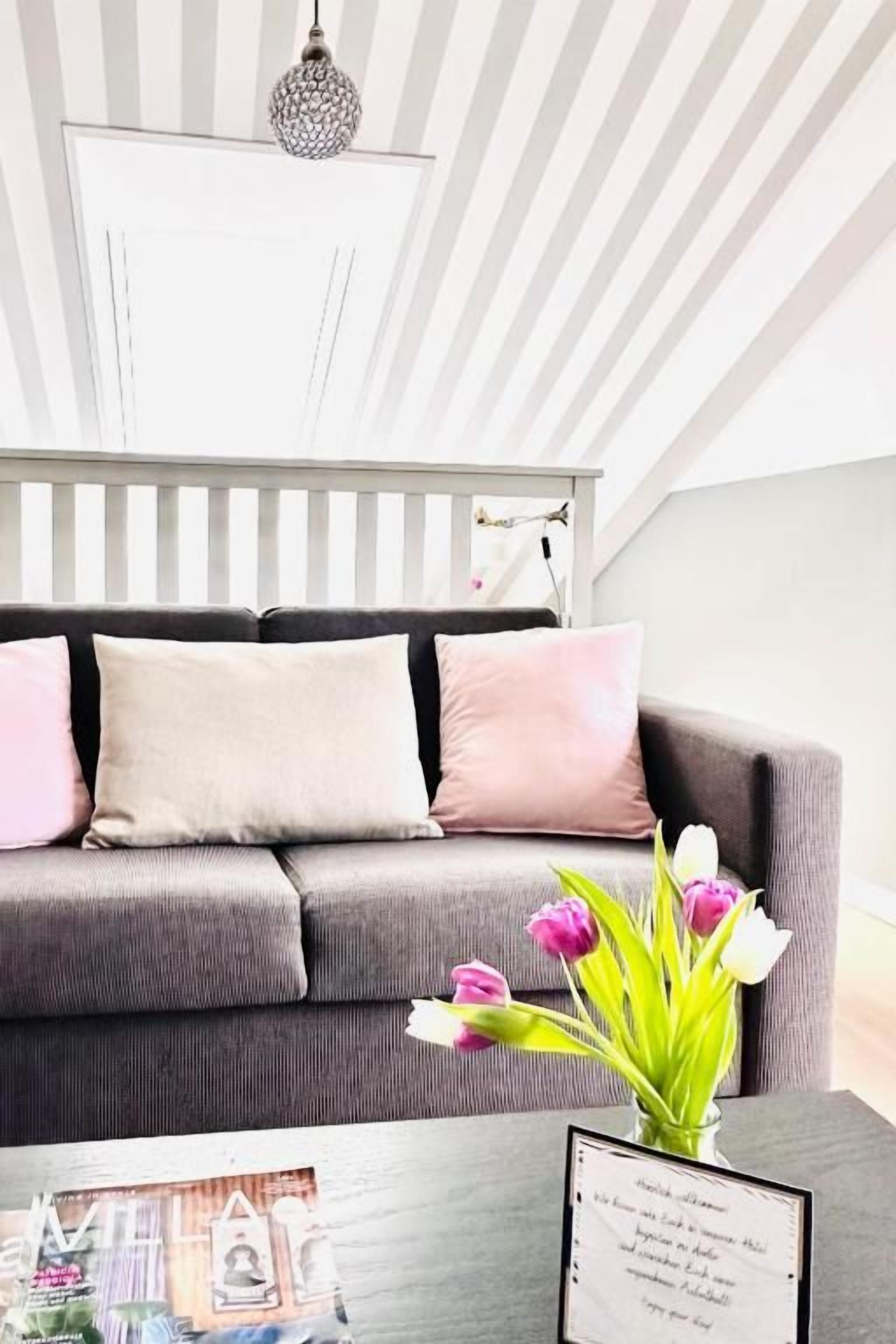 Een moderne woonkamer met een grijze bank, een vaas met bloemen en een lijst met een foto op een bijzettafeltje.